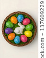 Colorful Easter eggs arranged around a white ceramic bunny in a woven basket filled with green grass on a light background, perfect for holiday celebrations 137609229