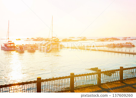 Jetty with yacht in marina on sunset. Sailboat at dock in evening at sea water. People walk on pier  137609260