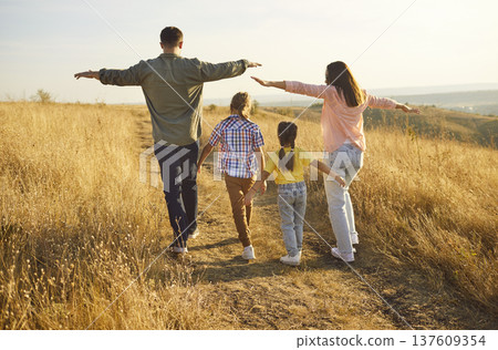 Happy family carefree walk with arms out in nature of golden hour, back view Happy family carefree walk with arms out in nature of golden hour, back view 137609354