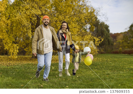 Happy family running in autumn park, parents and child with colorful balloons Happy family running in autumn park, parents and child with colorful balloons 137609355