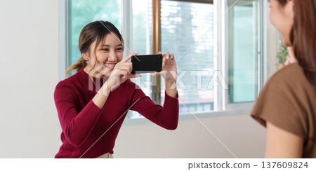 Capturing Smiles. Woman taking photo of her friend with smartphone. 137609824