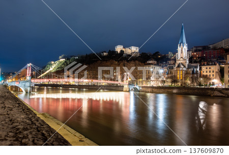 Lyon, france. December 29, 2023. Lyon cityscape at night showcasing the illuminated passerelle saint georges and saint georges church reflecting in the calm saone river 137609870