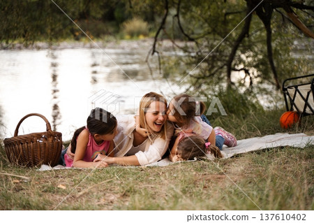 Happy family enjoying a picnic by the river having fun and kissing Happy family enjoying a picnic by the river having fun and kissing 137610402