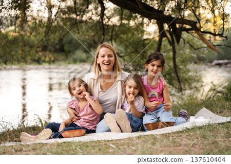Mother and daughters enjoying a picnic by the river 137610404