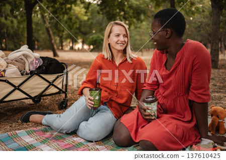 Two friends enjoying a picnic in the park, drinking and chatting 137610425