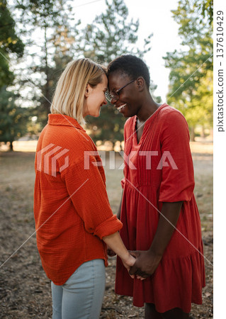 Two Smiling Women Holding Hands and Touching Foreheads in a Park 137610429