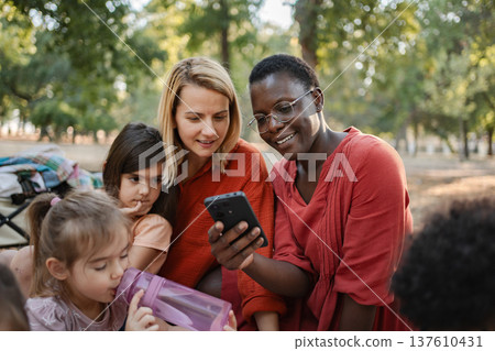 Teachers showing smartphone to preschool girls during school trip in a park Teachers showing smartphone to preschool girls during school trip in a park 137610431