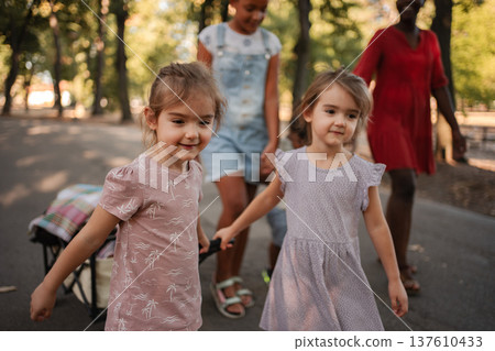 Children pulling cart with blanket in park with babysitters Children pulling cart with blanket in park with babysitters 137610433