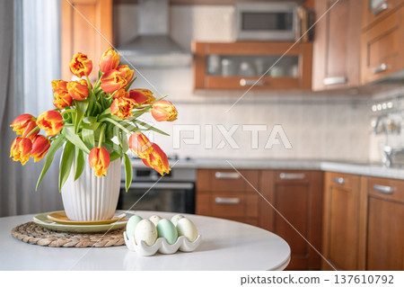 Easter tulips bouquet in white vase on kitchen table interior Easter tulips bouquet in white vase on kitchen table interior 137610792