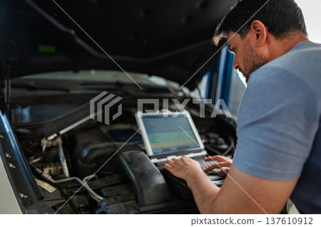 Mechanic using laptop diagnosing car engine problems in auto rep Mechanic using laptop diagnosing car engine problems in auto rep 137610912
