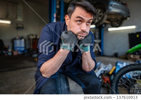 Bored mechanic resting chin on hands in garage Bored mechanic resting chin on hands in garage 137610913