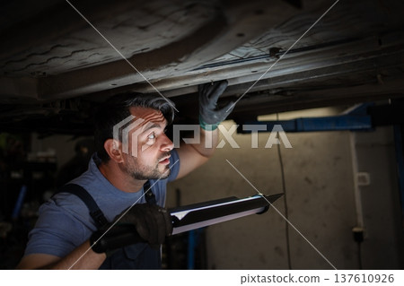 Mechanic inspecting car chassis with flashlight in garage 137610926