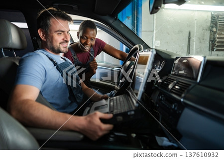 Mechanics performing diagnostics on a car's electronics using a computer Mechanics performing diagnostics on a car's electronics using a computer 137610932
