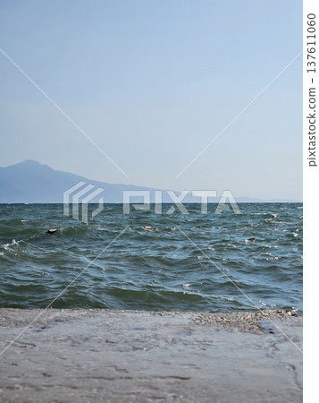 Picturesque view to blue sea and mountain island on horizon in mist. Calm water surface, background for traveling and vacation,Beautiful sea view, sailboats far away in the sea in sunny day. 137611060