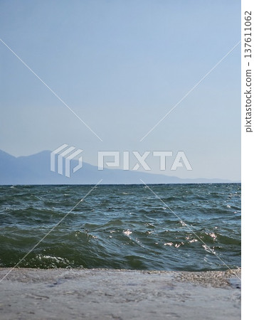 Picturesque view to blue sea and mountain island on horizon in mist. Calm water surface, background for traveling and vacation,Beautiful sea view, sailboats far away in the sea in sunny day. 137611062