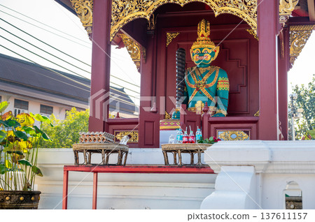 Green temple guardian statue with offerings of soda and eggs on table in front. Traditional Thai ritual symbolizing respect, faith, and blessings in sacred cultural and religious setting. 137611157