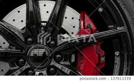 Black alloy wheel with red brake caliper and drilled disc rotor close-up detail of luxury sports car braking system 137611339