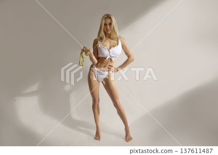 Fit blonde woman with measuring tape standing in lingerie, weight loss, body shaping and fitness diet concept 137611487