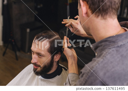 Barber cutting male client hair with scissors and comb. Close up of professional haircut process, precision technique, men grooming service in modern barbershop. 137611495