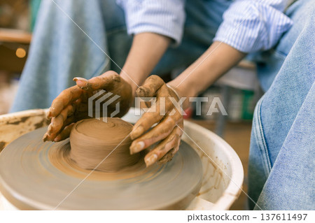 Close up of female hands shaping clay on pottery wheel in ceramic studio, handmade pottery process and traditional craft Close up of female hands shaping clay on pottery wheel in ceramic studio, handmade pottery process and traditional craft 137611497