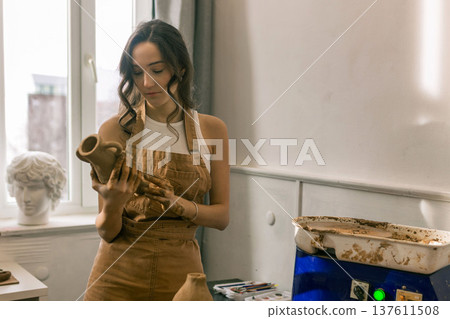 Young female ceramic artist holding handmade clay vase in pottery studio, creative craft process and handmade ceramics production Young female ceramic artist holding handmade clay vase in pottery studio, creative craft process and handmade ceramics production 137611508