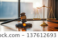 Wooden judge gavel and golden scales of justice standing on desk in modern lawyer office with bright sunlight window background representing legal system 137612693