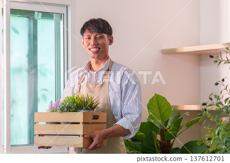 Sustainability in Gardening. A person smiling while holding a wooden crate of potted plants indoors. Sustainability in Gardening. A person smiling while holding a wooden crate of potted plants indoors. 137612701