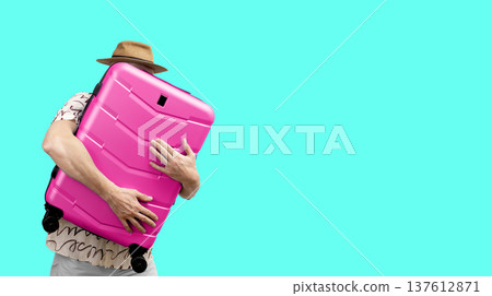 Man holding suitcase. Happy tourist in summer hat embraces large plastic carry-on pink bag. Holiday Man holding suitcase. Happy tourist in summer hat embraces large plastic carry-on pink bag. Holiday 137612871