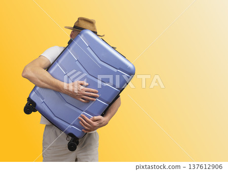Man in summer hat holding suitcase. traveler embraces giant travel bag in fun vacation mood. Funky 137612906