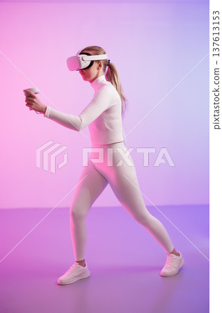 Woman in VR glasses walking in illuminated studio 137613153