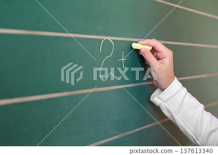 First grade pupil a girl writing on green blackboard at school lesson First grade pupil a girl writing on green blackboard at school lesson 137613340