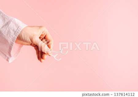 Hand holding a white dental floss pick on pink background, minimal oral hygiene concept with copy space Hand holding a white dental floss pick on pink background, minimal oral hygiene concept with copy space 137614112