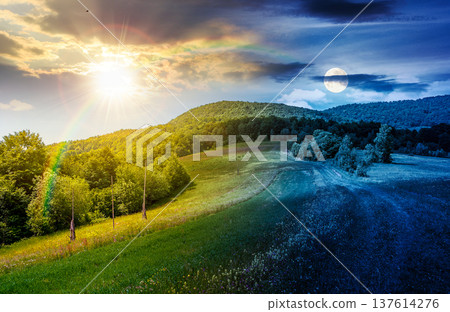grassy rural fields in mountain landscape. day meet night. sun and moon over country road to forest through rolling hills. beautiful picture of a scenery on summer solstice weather with clouds on sky 137614276