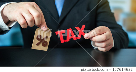A businessman holding the word Tax and a percentage sign. Business and finance concept. taxation, Taxes rates, fiscal policy, financial obligations, and economic regulation. Taxation A businessman holding the word Tax and a percentage sign. Business and finance concept. taxation, Taxes rates, fiscal policy, financial obligations, and economic regulation. Taxation 137614682