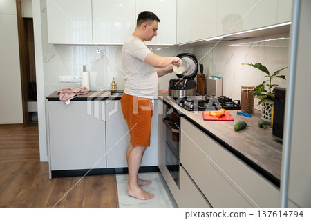 A young caucasian 35 old caucasian man and cook food in a slow cooker in the kitchen 137614794
