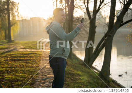 A happy young, beautiful brunette 35 old man takes a selfie while walking in a park 137614795