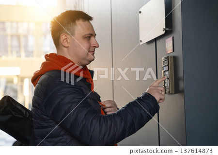Beautiful 35 year old caucasian man presses the apartment number or the code on the intercom. Beautiful 35 year old caucasian man presses the apartment number or the code on the intercom. 137614873