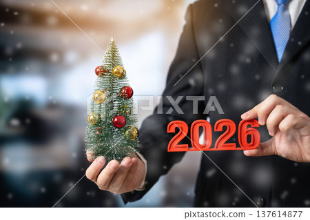 A businessman holds a Christmas tree and the numbers 2026. 137614877