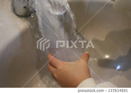 A child's hands holding a cup at the sink while gargling and washing their hands 137614891