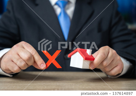 Businessman holding a prohibition sign over a house. Concept of real estate restrictions. 137614897