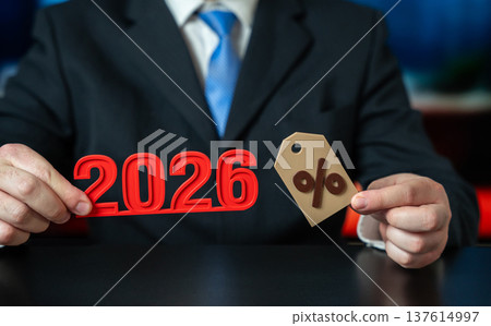 A businessman holding the numbers 2026 and a percent sign. Concept of business A businessman holding the numbers 2026 and a percent sign. Concept of business 137614997