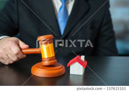 Male hand holds a judge gavel near house. 137615101