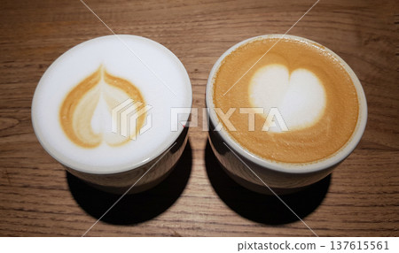 Two cups of coffee with heart designs sit on a wooden table duri Two cups of coffee with heart designs sit on a wooden table duri 137615561
