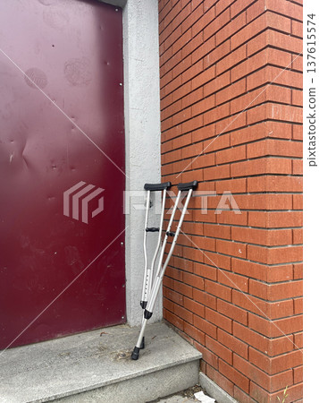 Crutches resting against the wall near a doorway on a cloudy day in a city setting Crutches resting against the wall near a doorway on a cloudy day in a city setting 137615574