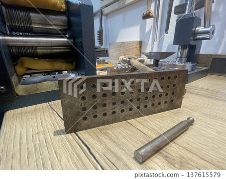 Metalworking jewelry tools are arranged on a wooden surface in a workshop, showing a metal plate  137615579