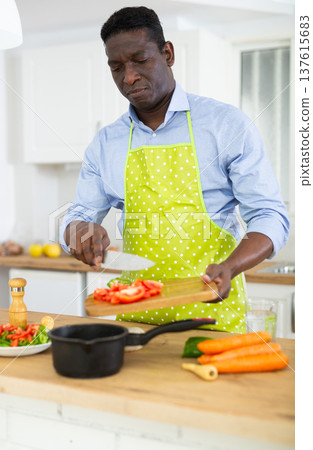 Man in apron making dinner at kitchen table Man in apron making dinner at kitchen table 137615683