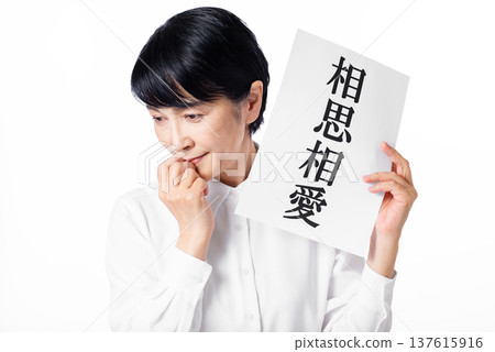 A senior woman wearing a white shirt shyly holding a piece of paper that says "Mutual Love" A senior woman wearing a white shirt shyly holding a piece of paper that says "Mutual Love" 137615916