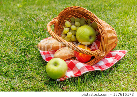 Picnic basket with fruits, and baguette on a sunny green meadow 137616178