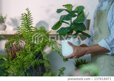Sustainability in Gardening. A person holding a potted plant in a green indoor space. Sustainability in Gardening. A person holding a potted plant in a green indoor space. 137618971