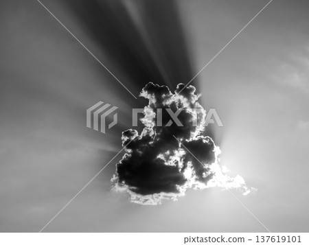 Sun rays from the evening sun behind small cloud. Black and white image. Sun rays from the evening sun behind small cloud. Black and white image. 137619101